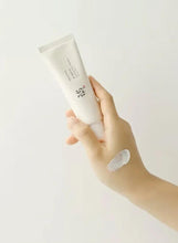 Hand holding face sunscreen tube with a white cream dollop on skin.
