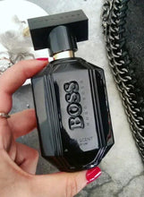 Hand holding black HUGO BOSS parfum bottle with gold-toned spray top on light surface
