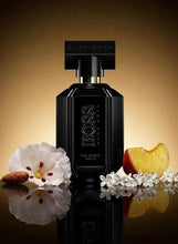 Black spray perfume bottle with white flowers and fruit accents against gold background