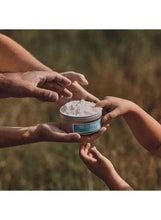 L’Occitane body cream jar held with hands, open lid showing white cream