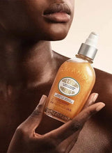 Almond shimmering body oil bottle held in hands, amber-gold liquid