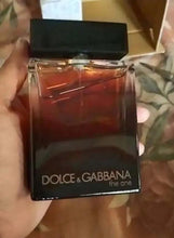 Men's eau de parfum bottle in hand, black base with amber liquid and clear top