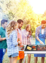 Portable charcoal BBQ grill with food cooking on metal grates, silver frame