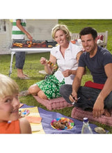 Portable charcoal BBQ grill with grilled food on grates and side shelf