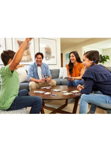 People playing a rummy-style card game with number cards on a coffee table