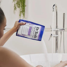 Dr Teal's lavender Epsom bath salt pouch held over a bathtub