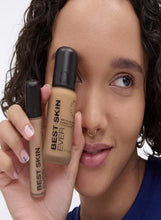 Liquid foundation bottles held near face, medium-dark neutral shade