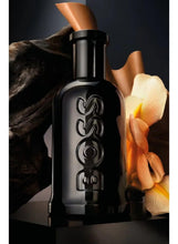 Black eau de parfum bottle with metallic cap, shown with orange and cream flowers