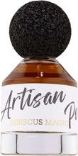 Perfume bottle close-up with black cap; amber liquid; label 'Artisan' and 'Hibiscus Magic'