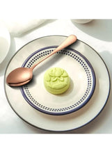 Rose gold stainless steel spoon on a plate beside a dessert