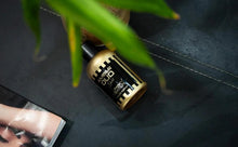 Amber Oud Gold eau de parfum bottle on dark surface with green leaves