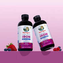 Two vegan liquid iron supplement bottles, berry flavor, with fruit berries nearby.