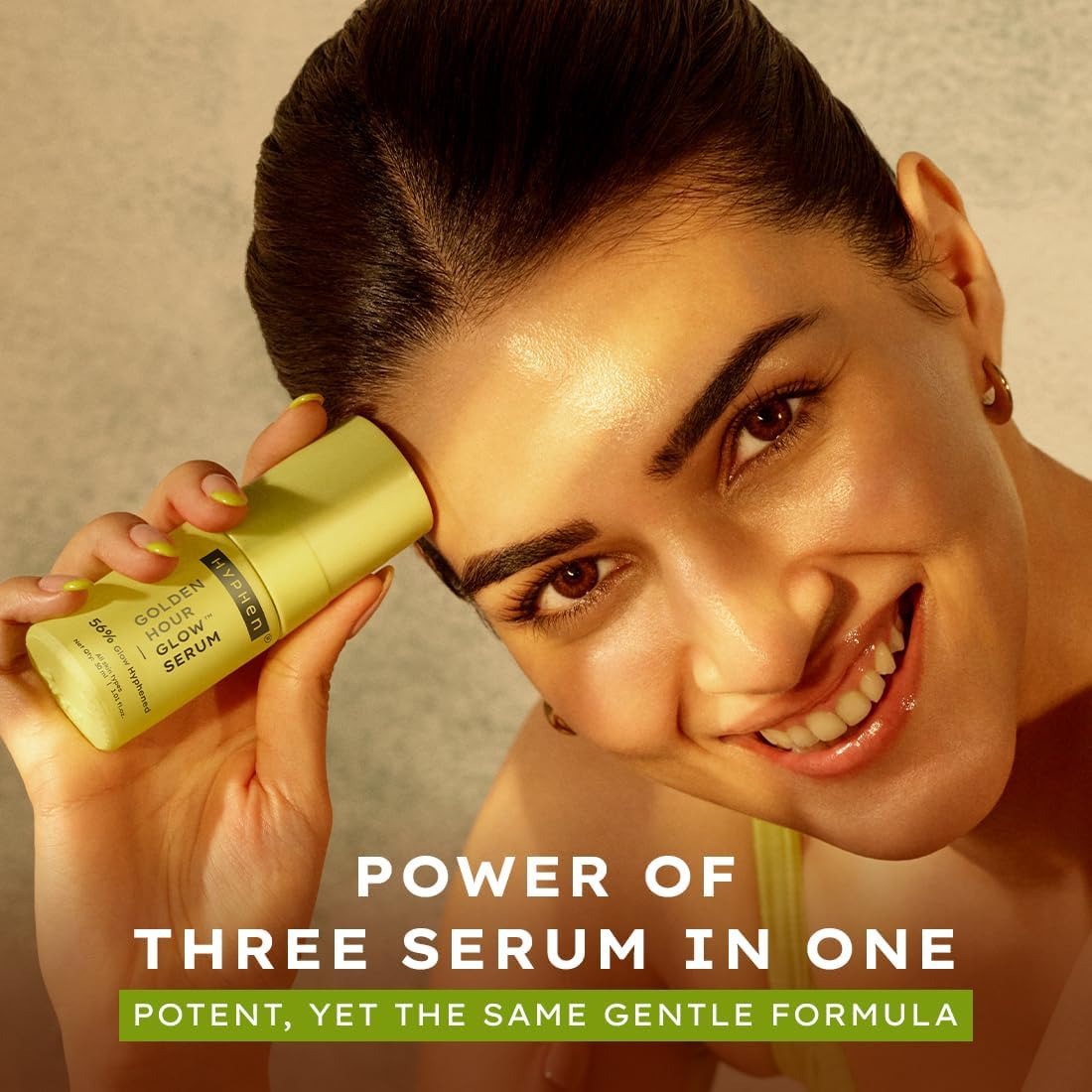 Hyphen Golden Hour Glow face serum bottle held near cheek, lime green cap