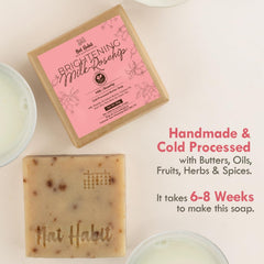 Square beige soap bar with speckled flecks, near pink branded box
