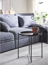 Round black side table with tray top and three legs holding a potted plant