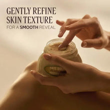 Almond body paste jar held by hands with fingers scooping from lid