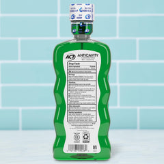 ACT Anticavity Fluoride Rinse green bottle back label showing drug facts and dosing cap on tiled bathroom counter