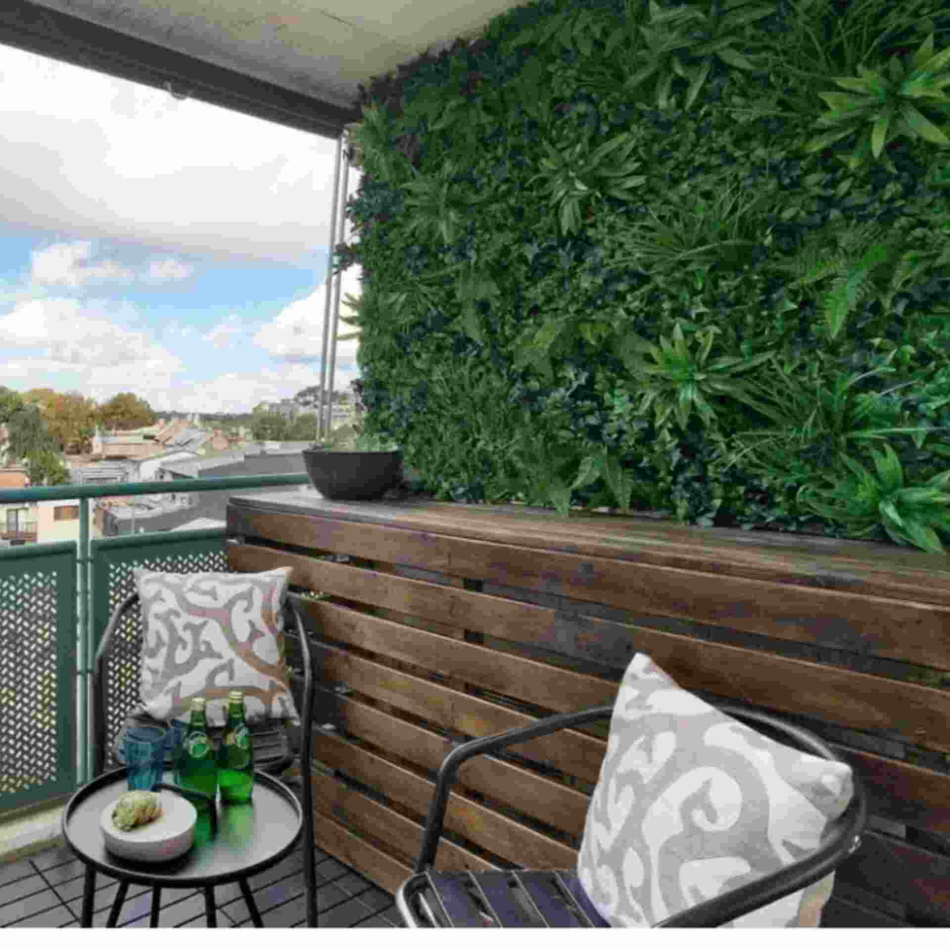 Huitich artificial grass wall backdrop installed on balcony with wooden bench and chairs