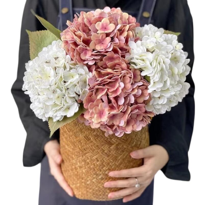 Hand holding woven basket with artificial pink hydrangea flower and white silk blooms