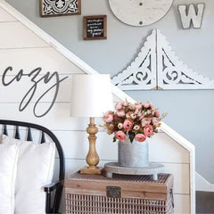 Artificial pink rose bouquet in rustic metal vase displayed on wooden chest next to lamp in cozy bedroom