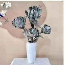 Artificial blue-gray rose bouquet in a white vase with dark leaves