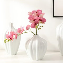 Pink artificial red rose flowers in a white decorative vase on a white table for home decor