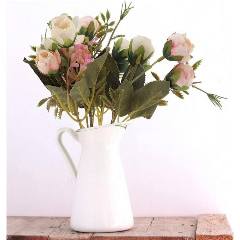 Huitich artificial rose flower bunch in white pitcher vase with green leaves on wooden surface