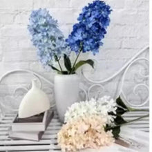 Artificial blue and cream flower bouquet in white vase on ledge