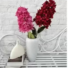 Artificial red flower stems with clustered blossoms in white vase