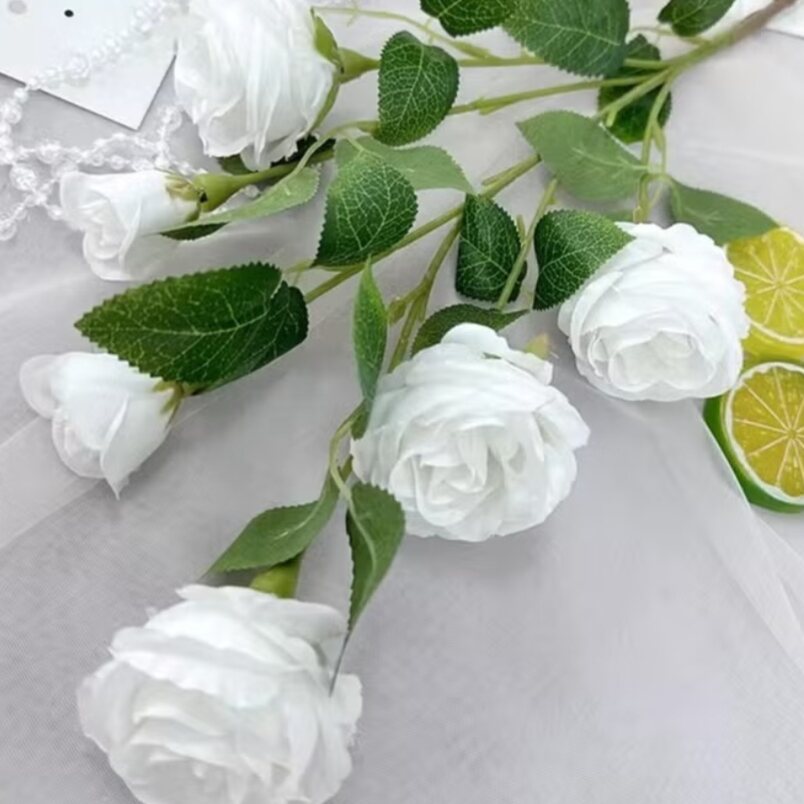 White artificial rose flowers for home decor by Huitich with green leaves on a light background