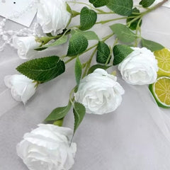 White artificial rose flowers for home decor by Huitich with green leaves on a light background