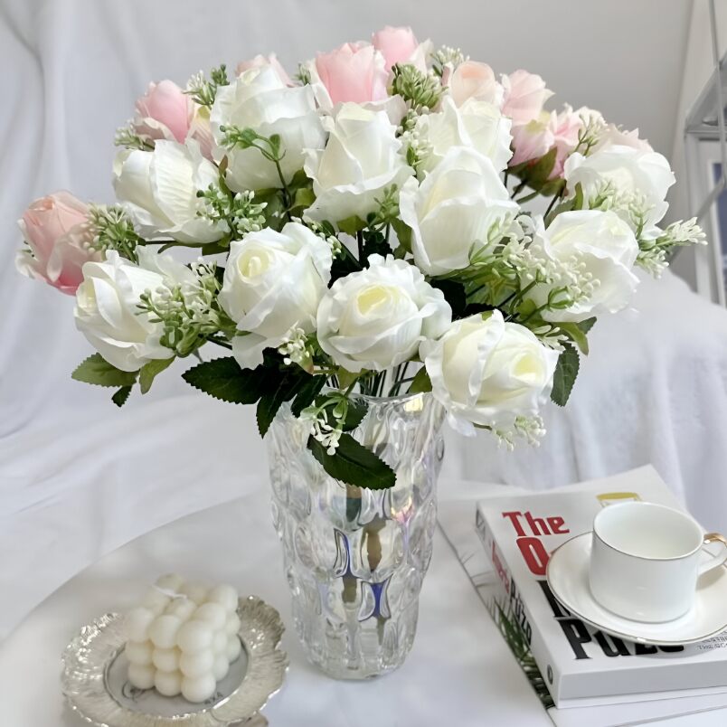 Huitich artificial white flower arrangement with pink accents in a clear textured vase on a white table