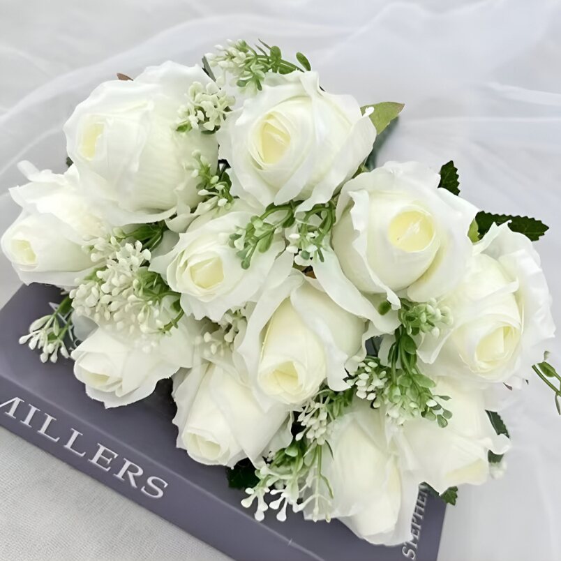 Huitich artificial white flower arrangement with realistic white roses and green foliage on a book