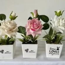 Artificial pink rose in white pot, with nearby white blooms in decorative pots