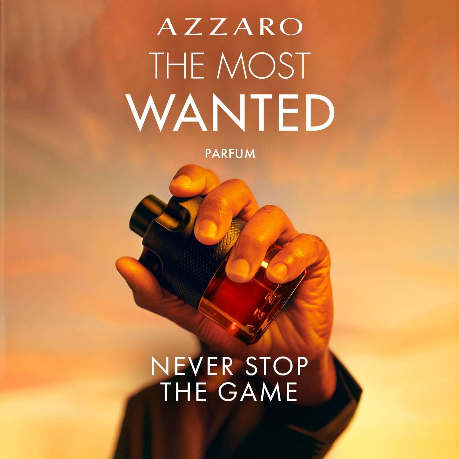 Hand holding Azzaro The Most Wanted Parfum for men bottle with warm sunset background