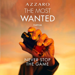 Hand holding Azzaro The Most Wanted Parfum for men bottle with warm sunset background