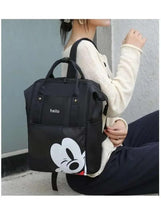 Black baby travel bag with 'hello' logo and cartoon face, worn with top handle and shoulder strap