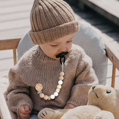 Baby in beige knit hat wearing a wooden and silicone beaded baby pacifier clip set attached to sweater