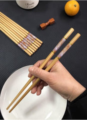Huitich bamboo chopsticks reusable set with decorative handles held over a white plate