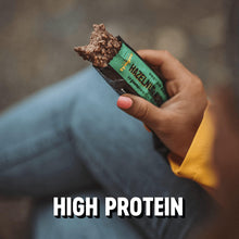 Hazelnut & nougat protein bar in green-and-black wrapper held in hand with bite