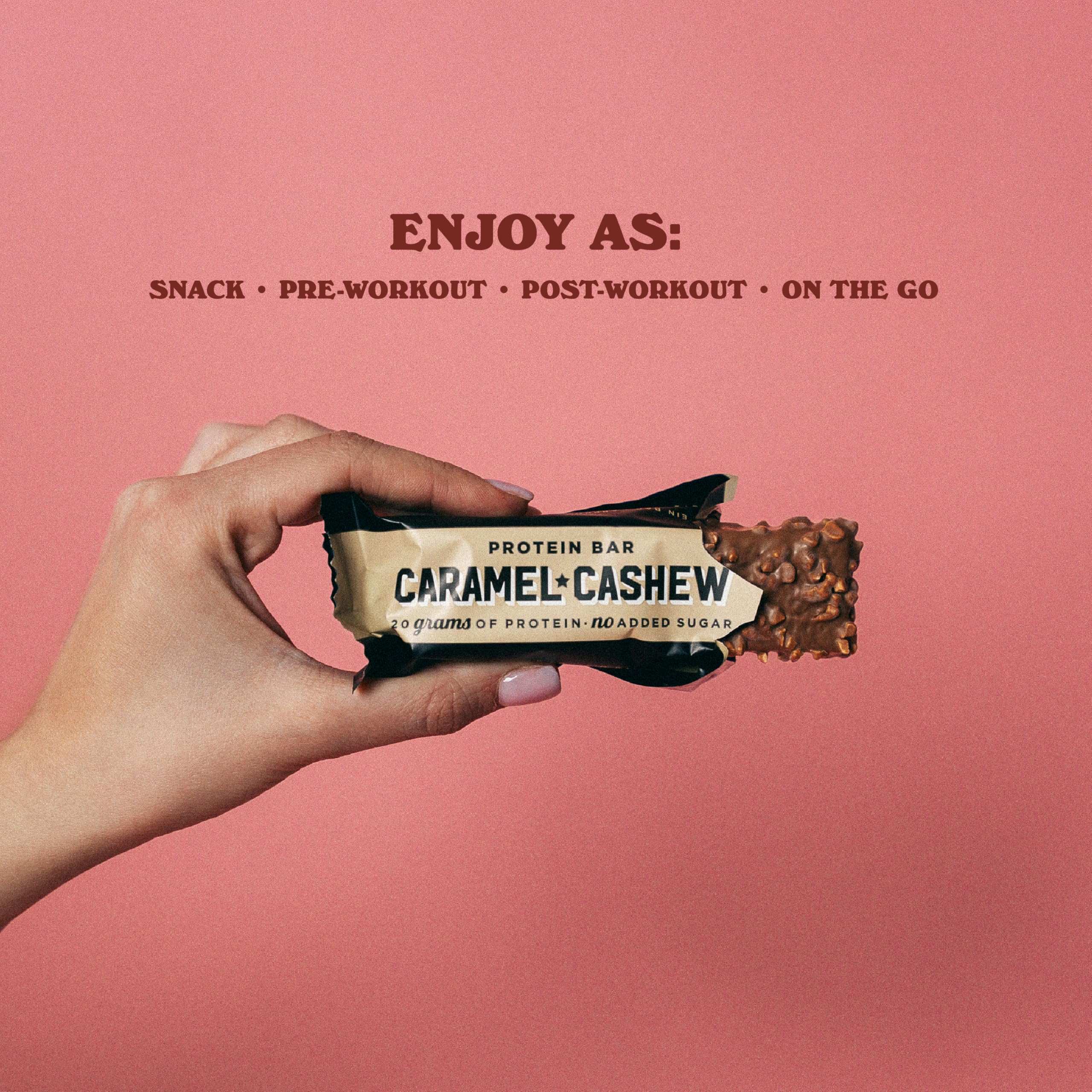 Hand holding partially unwrapped Barebells protein bars caramel cashew with crunchy nut coating on pink background
