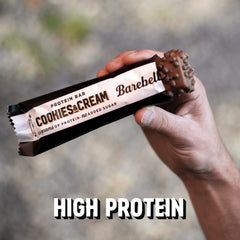 Barebells high protein cookies and cream bar partially unwrapped held in hand showing chocolate coating and crunchy bits