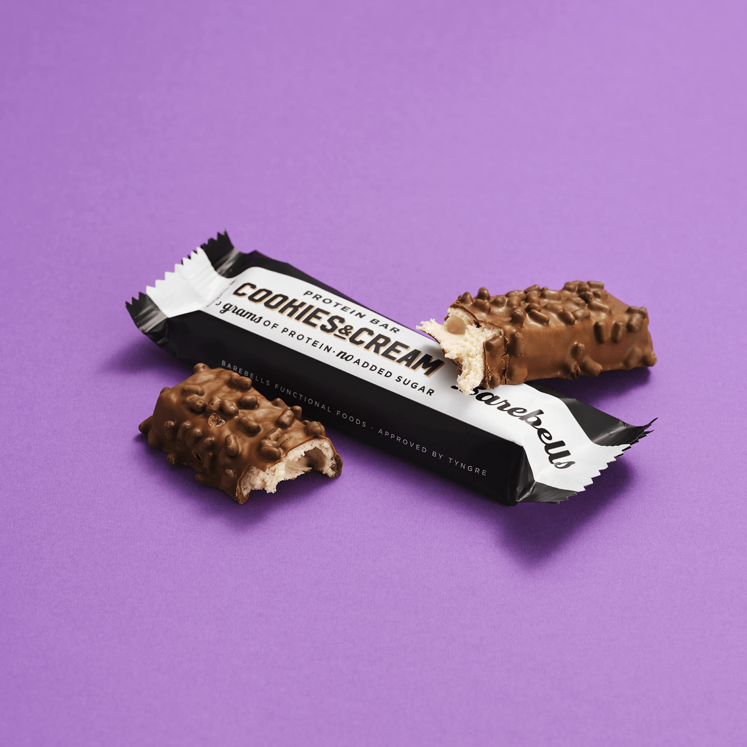 Barebells high protein cookies and cream bar chocolate coated with crunchy bits and creamy filling on purple background