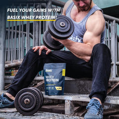 Basix vanilla whey protein powder UAE pouch beside dumbbells as muscular man performs bicep curl on metal steps