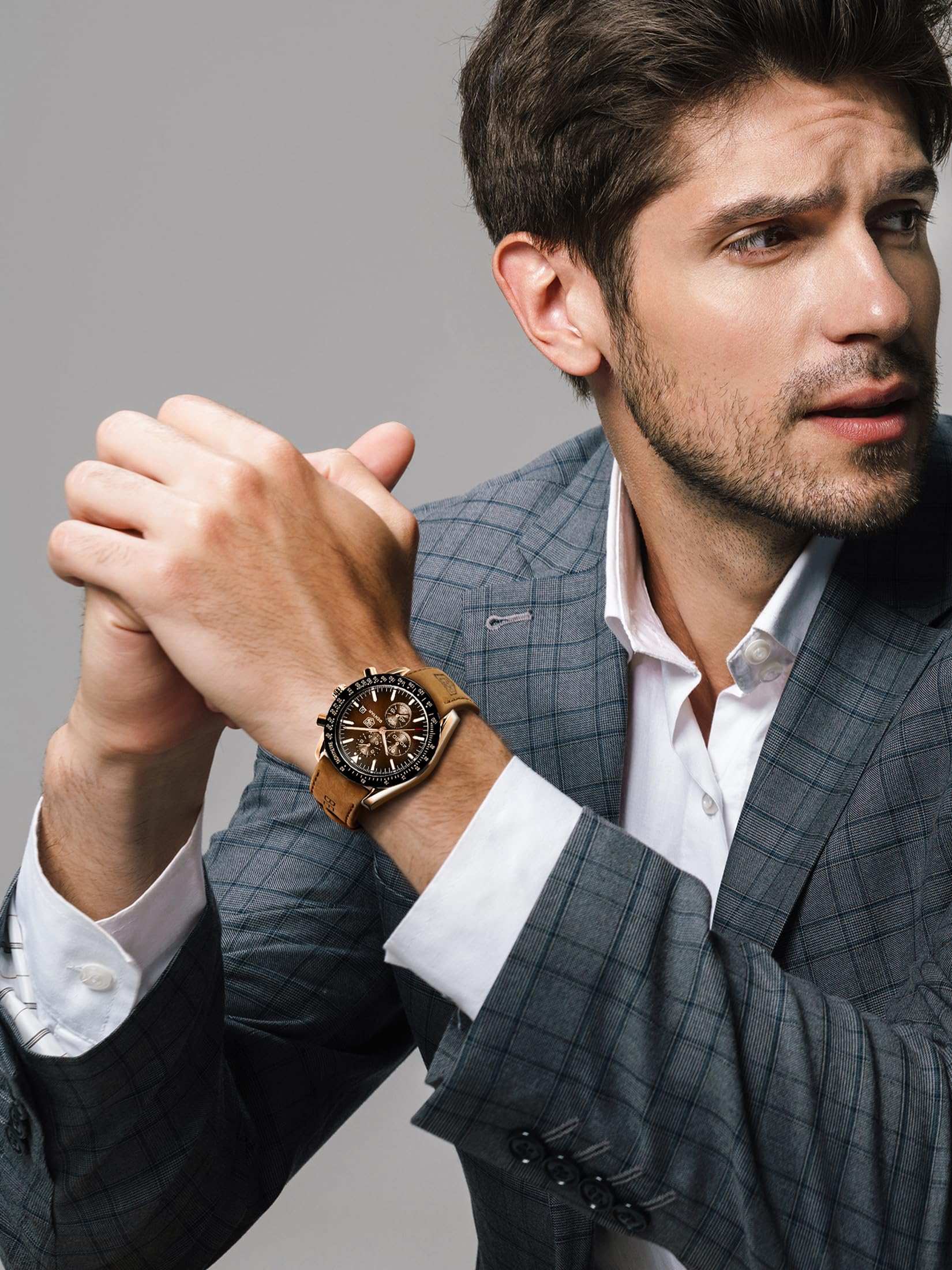 Business casual analog watch for men worn by a man in a gray checkered suit posing with clasped hands