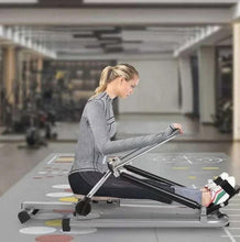 Rowing machine in use on floor; woman rowing on black seat