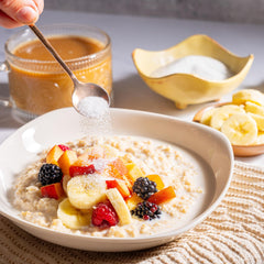 Hand sprinkling BetterBody Foods monk fruit blend over warm oatmeal topped with banana, peach, and berries