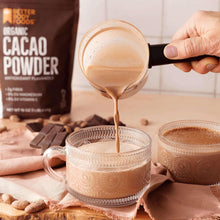 Cacao powder being poured into a glass mug, with chocolate bars and cookies