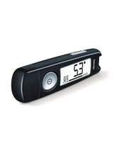 Handheld blood glucose monitor with digital display and circular control button.