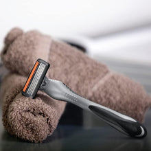 Disposable razor with silver head and black grip lying on a brown towel